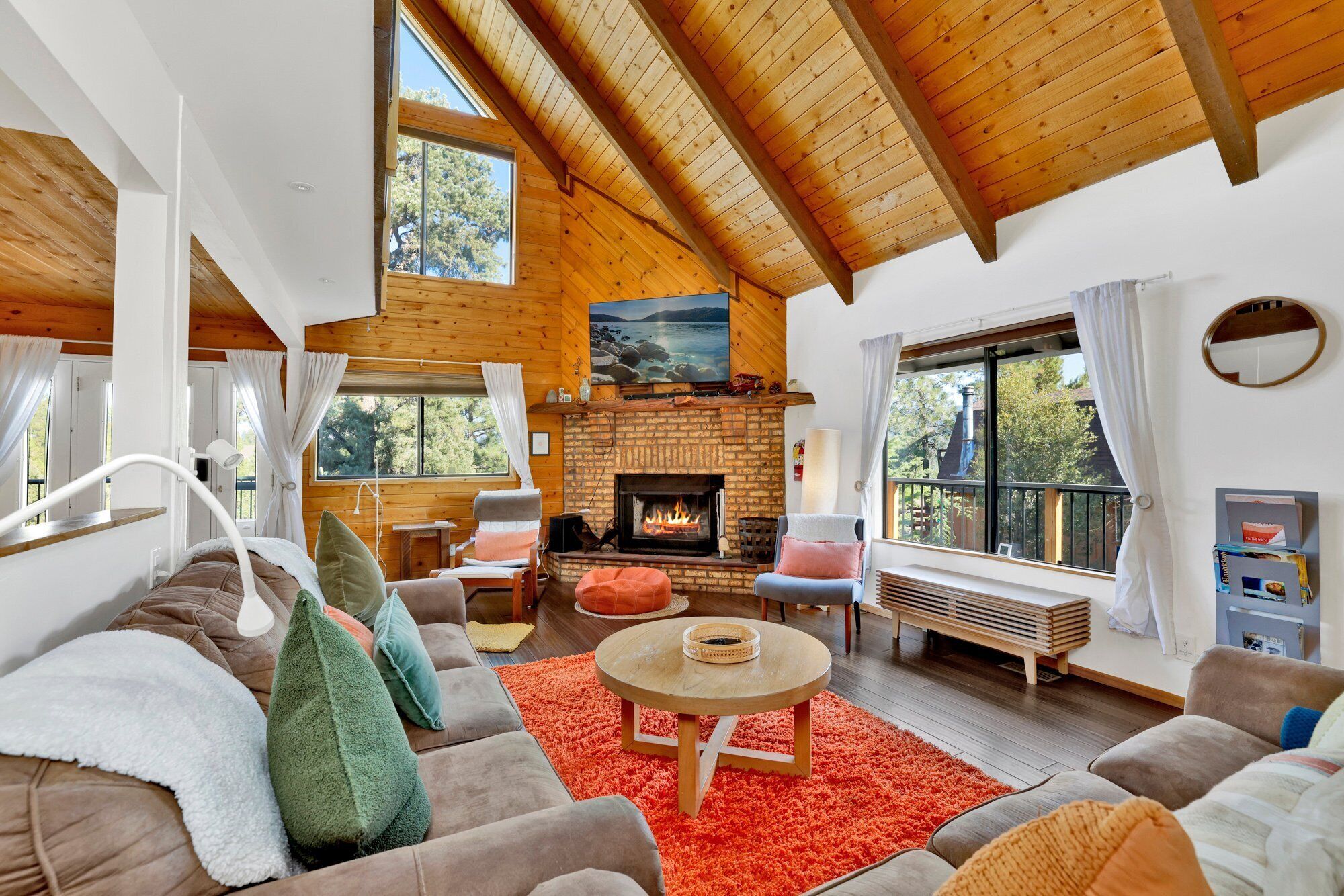 A cozy living room with a fireplace, wooden beams, and large windows.