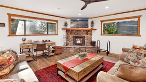 A cozy living room with a fireplace, a ceiling fan, and a large window. - Elmwood Place #2218 (Big Bear City)