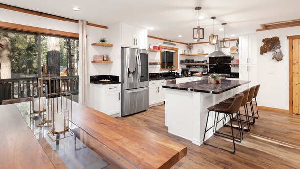 A modern kitchen with a large island, stainless steel appliances, and a wooden dining area with bar stools. - Elmwood Place #2218 (Big Bear City)