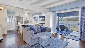 A modern kitchen with white cabinets and stainless steel appliances, a grey sofa with patterned cushions, and a view of a lake through a sliding glass door. - North Shore Chalet #2173 (Fawnskin)