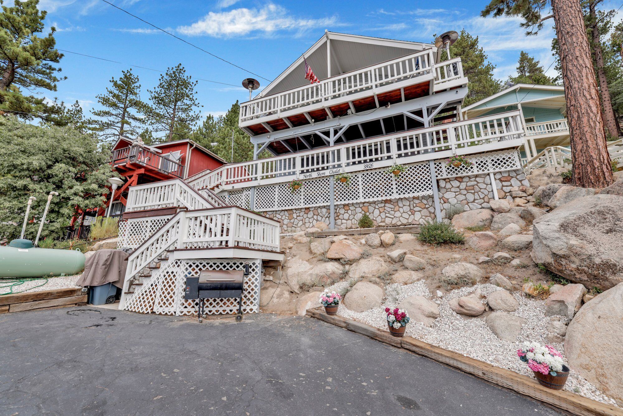 A multi-story building with a stone facade, wooden balconies, and a parking area with a barbecue grill.