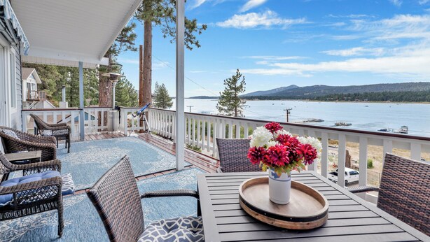 A covered outdoor seating area with wicker furniture, a table with a tray, and a vase of flowers. - North Shore Chalet #2173 (Fawnskin)