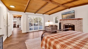 A bedroom with a wooden ceiling, a fireplace, a bed with a plaid bedspread, and a view of a balcony with a door leading outside. - Splash Mountain #1904 (Big Bear Lake)