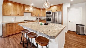 A kitchen with wooden cabinets, stainless steel appliances, and a granite island with bar stools. - Splash Mountain #1904 (Big Bear Lake)