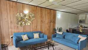 Un soggiorno con due divani blu, un tappeto decorato, pareti rivestite in legno e un'area cucina sullo sfondo.