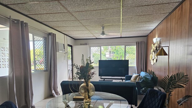 Un soggiorno moderno con un tavolino in vetro, divani blu scuro, una TV a schermo piatto e una ventola a soffitto.