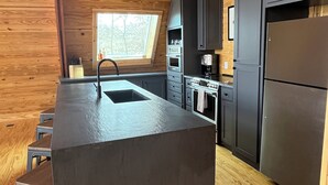 A modern kitchen with a central island, wooden flooring, and built-in appliances. - Modern lakefront cabin nestled in the piney woods of East Texas. Pet Friendly! (Pittsburg)