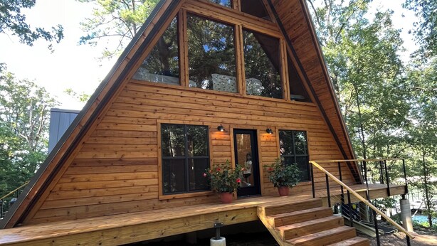 A wooden triangular house with a large window, a staircase, and potted plants. - Modern lakefront cabin nestled in the piney woods of East Texas. Pet Friendly! (Pittsburg)