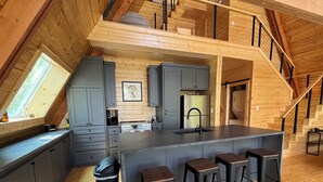 A modern kitchen with a central island, grey cabinets, and a wooden floor. - Modern lakefront cabin nestled in the piney woods of East Texas. Pet Friendly! (Pittsburg)