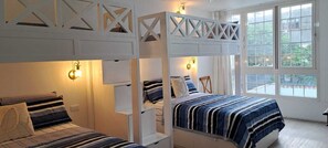 Quarto com beliches, janela com cortinas e luminárias fixadas na parede.