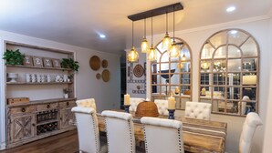 A dining area with a wooden table, white upholstered chairs, hanging pendant lights, and a mirror above the table. - Casa Ramos Salamanca (Lima)