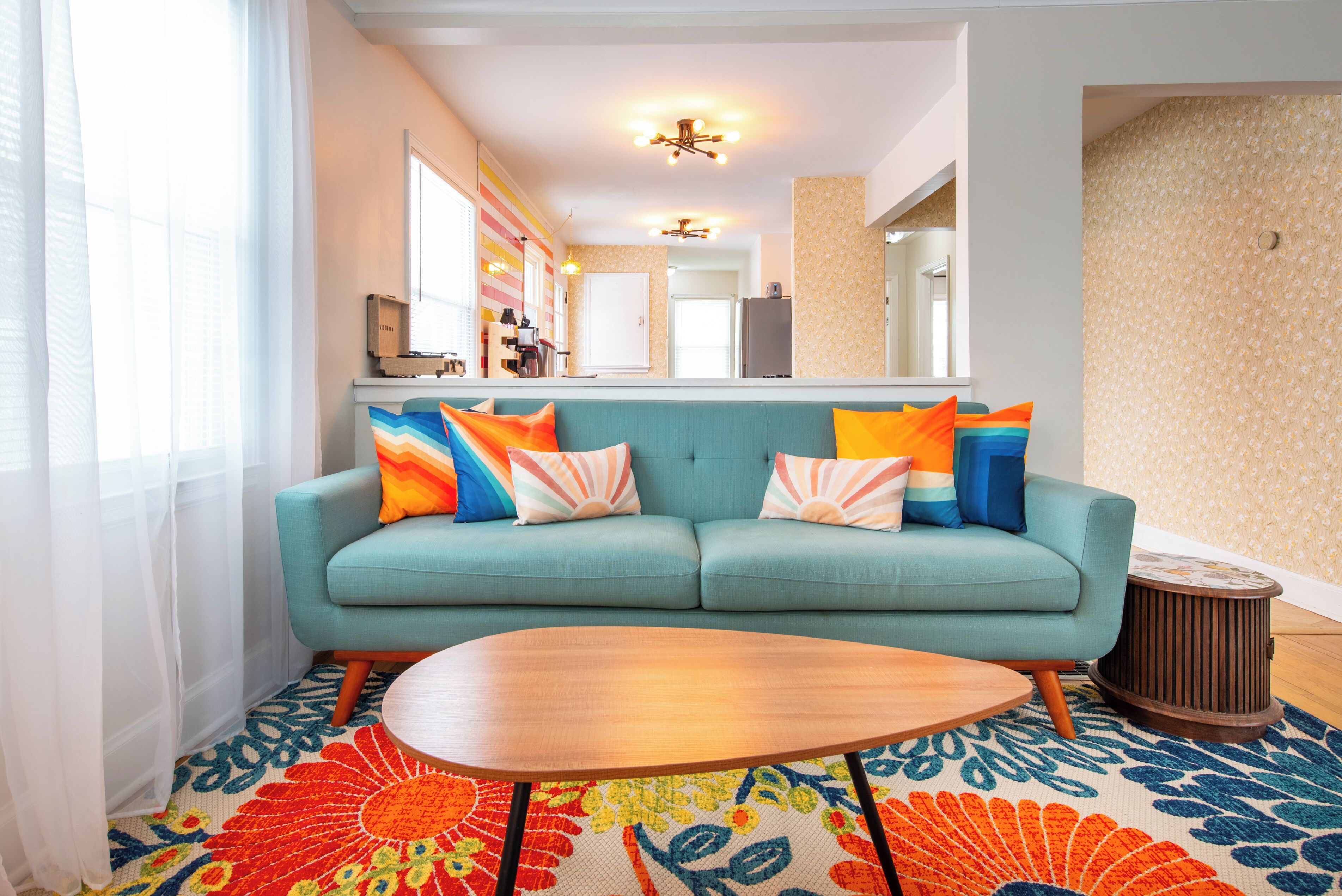 A living room with a teal sofa, colorful pillows, a wooden coffee table, and a patterned rug.