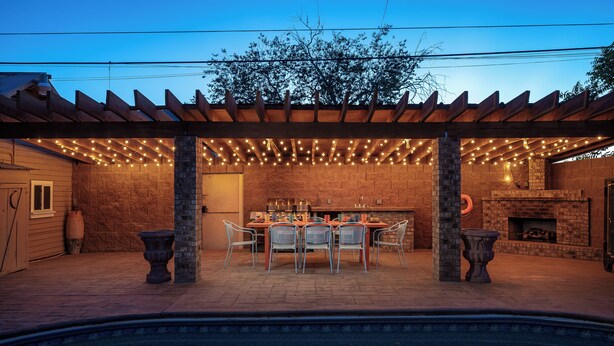 Eine Terrasse im Freien mit Pool, Kamin aus Ziegelsteinen und Lichterketten.