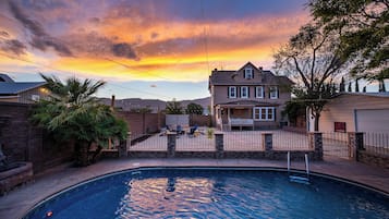 Piscina residencial con una casa al fondo, rodeada por un muro de ladrillo y palmeras.