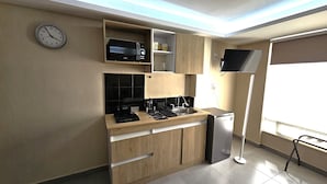 Cocina compacta con microondas, estufa y refrigerador, muebles de madera y un reloj en la pared.