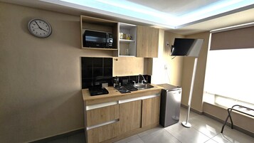 Cocina compacta con microondas, estufa y refrigerador, muebles de madera y un reloj en la pared.