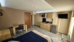 Habitación de hotel pequeña con cama, escritorio, kitchenette y televisor.