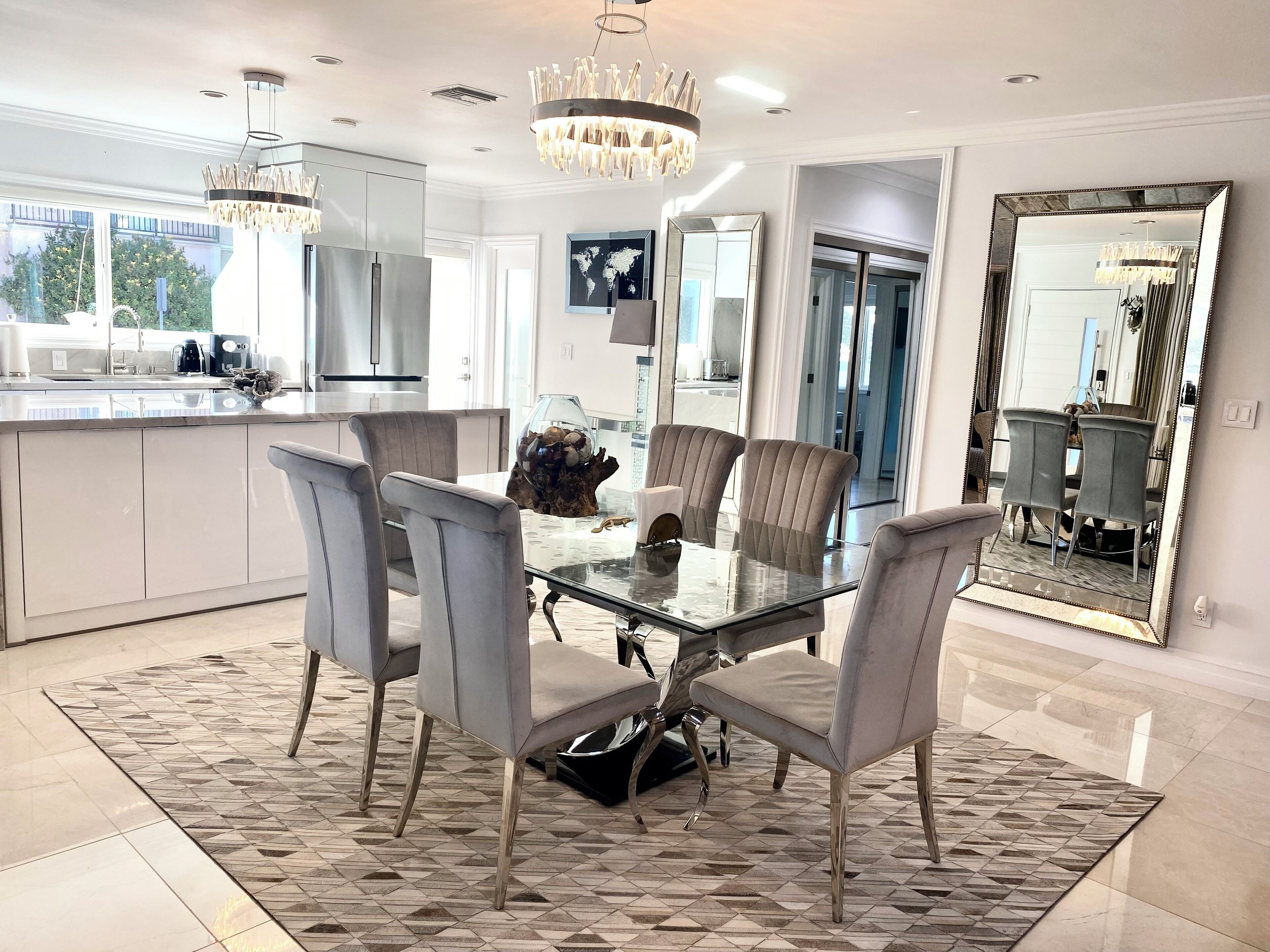A modern kitchen with a glass dining table, grey upholstered chairs, and a decorative centerpiece.