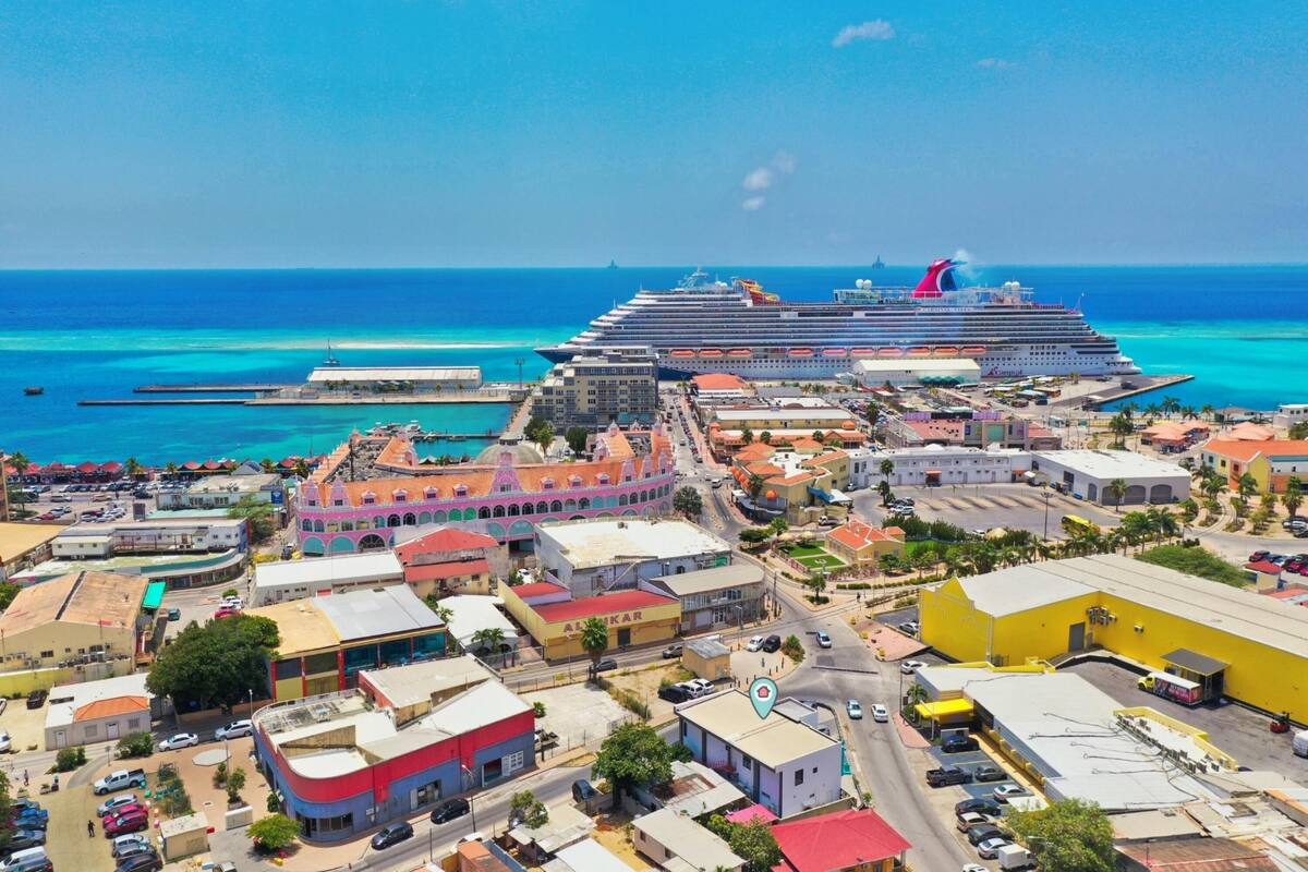 Un crucero amarrado en un puerto con edificios coloridos y un mar azul claro al fondo.