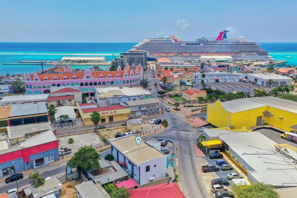 Un paisaje urbano costero con un gran crucero anclado en el puerto, edificios coloridos y una vista despejada del océano.