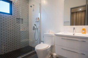 A modern bathroom with a glass shower enclosure, a white toilet, and a sink with a mirror above it. - Downtown Oranjestad Apartments & Studios (Oranjestad)
