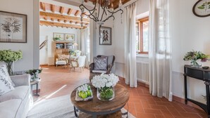 A spacious living room with a wooden ceiling, a chandelier, a dining area, and a view of the outdoors. - Grumo Farmhouse in Pescaglia (Pescaglia)