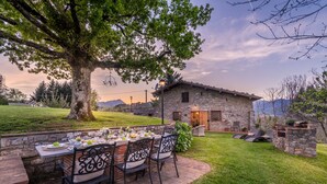 A stone building with a dining area set up outdoors, featuring a table with chairs and a view of the surrounding landscape. - Grumo Farmhouse in Pescaglia (Pescaglia)