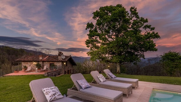 A poolside area with lounge chairs and a stone building in the background. - Grumo Farmhouse in Pescaglia (Pescaglia)