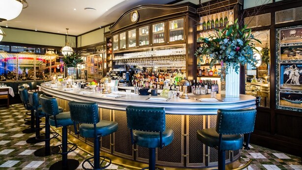 A bar area with a curved counter, multiple stools, and a large display of bottles. - Chestnut Blossom 1 Bedroom in Kensington (London)