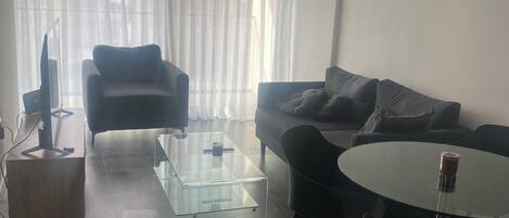 A modern living room with a sofa, a glass coffee table, a round table, and a TV stand.