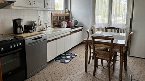 Una cucina compatta con mobili bianchi, un fornello, lavastoviglie, forno a microonde e un tavolo da pranzo con sedie.