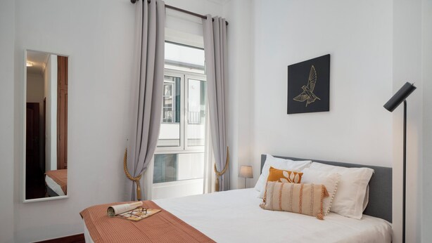 A hotel room with a large bed, a window with curtains, a mirror, a wall-mounted artwork, and a bedside lamp. - In the centre of Funchal - Apartamento do Carmo I (Funchal)