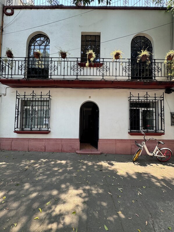 A two-story building with a balcony, a bicycle parked in front, and a door leading to the entrance. - Casa Alquimia Condesa (Mexico City)