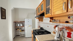 Una cocina con armarios de madera, microondas, refrigerador, estufa y pileta.