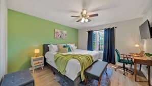 Un dormitorio con cama, mesita de noche, lámpara, escritorio, silla y ventilador de techo.