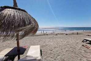 A beach with a thatched umbrella, a lounge chair, and a sandy shore.