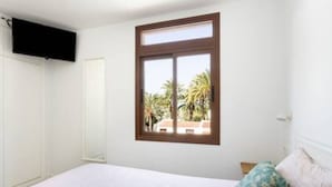 A bedroom with a bed, a window with a view of palm trees, and a TV mounted on the wall. - Home2Book Charming Apt Costa Adeje, Pool&Terrace (Playa de las Americas)