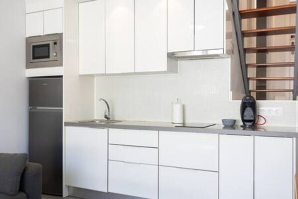 A modern kitchen with white cabinets, a stainless steel microwave, a coffee machine, and a small sink.