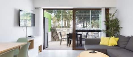 Un salon moderne avec un canapé, une table basse et un téléviseur. Il y a un balcon avec une table et des chaises.