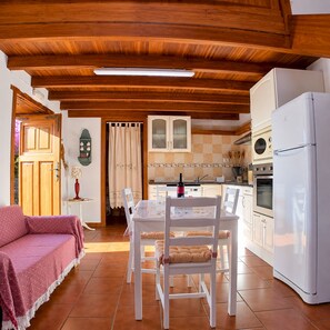 A cozy kitchen with wooden beams, a dining table with chairs, a refrigerator, and a stove. - La Pestilla 2 - Stunning rustic house, El Hierro (Taibique)