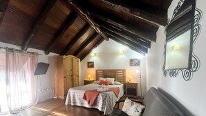 Un dormitorio acogedor con techo de madera, una cama con colcha a rayas, una mesita de noche con lámpara y un espejo grande en la pared.