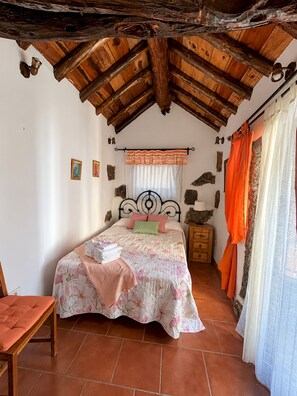 A bedroom with a wooden ceiling, a bed with floral bedding, a nightstand, and a chair.