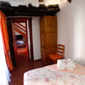 A bedroom with a wooden wardrobe, a chair, a bed with a floral bedspread, and a TV in the background. - La Pestilla 2 - Stunning rustic house, El Hierro (Taibique)