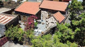 Una zona residencial con varias casas, cada una con tejados de tejas rojas. Se observan muros de piedra y algo de vegetación alrededor de las casas.