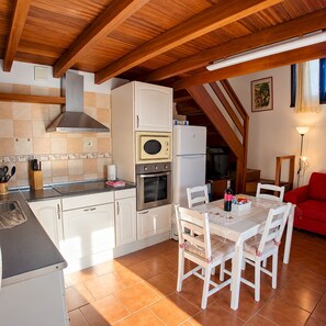 A kitchen with white cabinets, a stove, oven, and a refrigerator. There is a dining table with chairs and a red sofa in the background. - La Pestilla 2 - Stunning rustic house, El Hierro (Taibique)