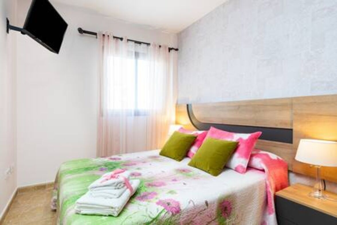 Habitación de hotel con cama, almohadas, mesita de noche, lámpara y ventana con cortinas.