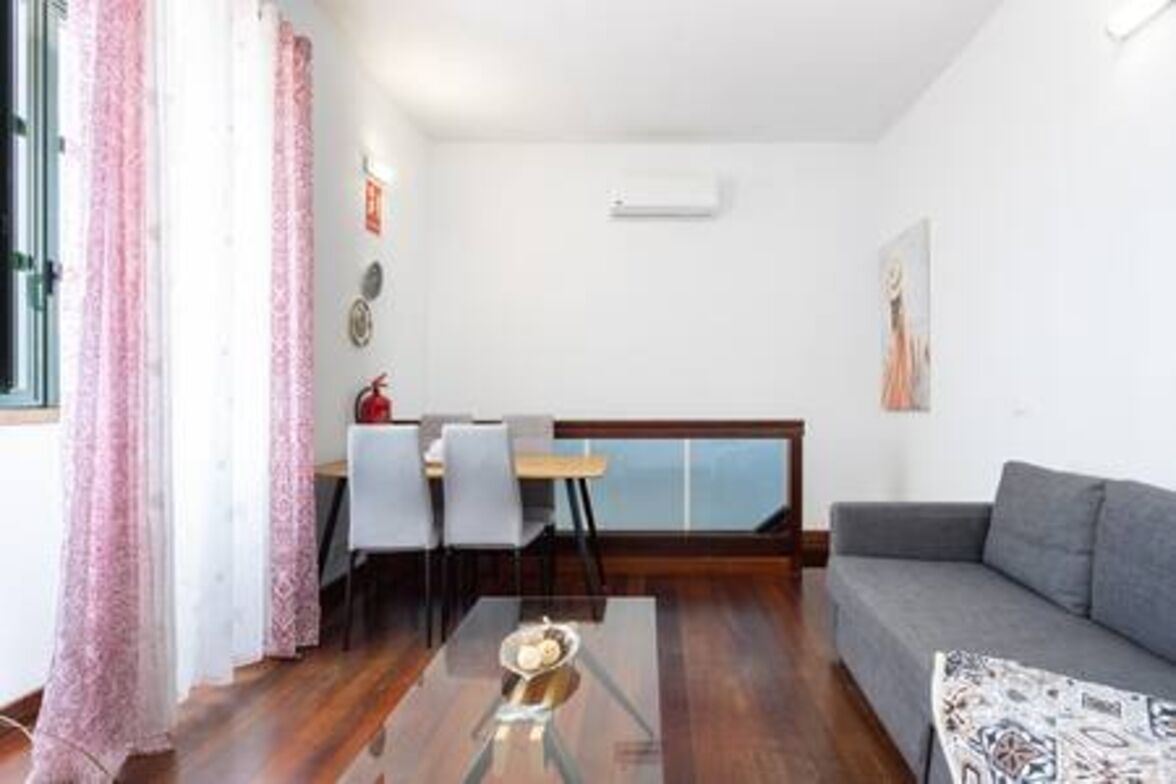 Una sala de estar moderna con un sofá gris, una mesa de centro de vidrio y un comedor con mesa y sillas.