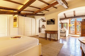 Un dormitorio con cama, vigas de madera, televisor, mesa y vistas a través de un arco.