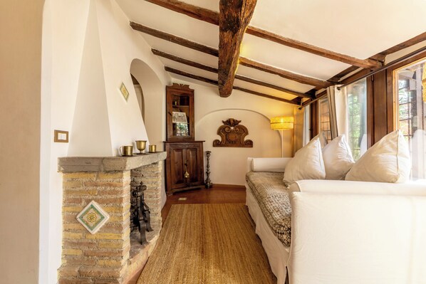 A cozy room with exposed wooden beams, a fireplace, a sofa, and a lamp.