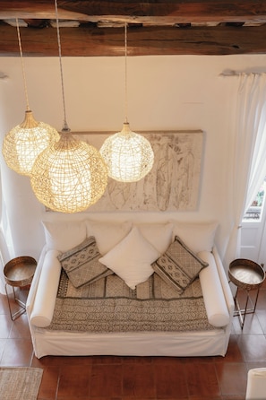 A cozy room with a sofa, patterned cushions, hanging woven light fixtures, and a marble wall.